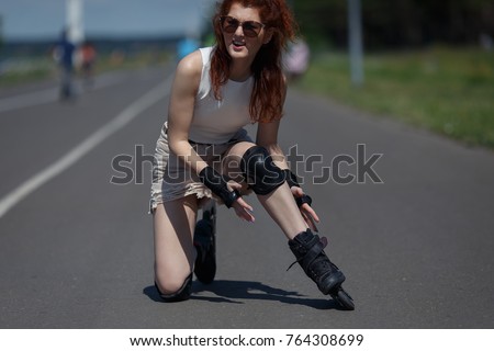 Beautiful young red-haired girl fell on the road and bruised her knee during skating on warm sunny day