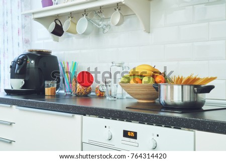 Interior of a light kitchen in the apartment. Bright home interior decoration items, fruit, flowers in a pot, steel hood. Bright ready-made picture for your individual design