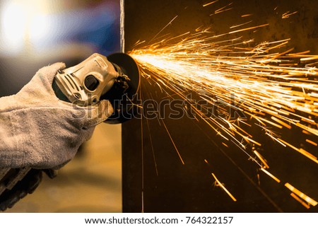 Worker using electric wheel grinding on steel structure in factory.