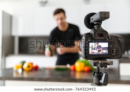 Close up of a video camera filming young smiling male blogger at the kitchen Royalty-Free Stock Photo #764323492