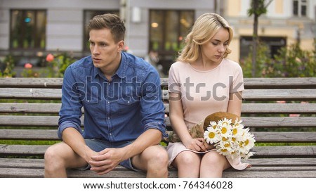 Unhappy couple sitting after fight, girl with flowers, problem in relationship Royalty-Free Stock Photo #764346028