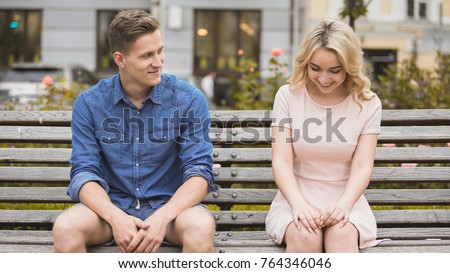 Shy blonde girl smiling, attractive guy flirting with beautiful woman on bench Royalty-Free Stock Photo #764346046