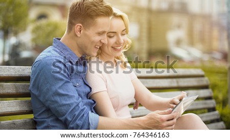 Smiling couple in love viewing photos from vacation on tablet, using mobile app