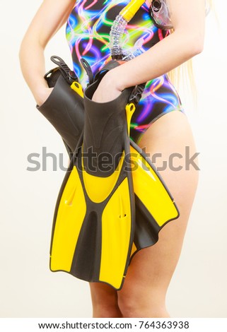 Female body wearing swimsuit holding flippers, studio shot on grey. Girl preparing to summer vacation. Snorkeling swimming concept