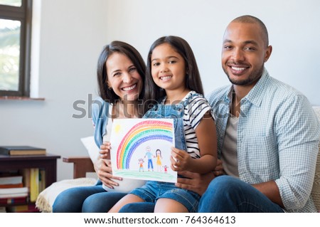 Smiling daughter showing painting of family with parents and beautiful rainbow. Happy child showing drawing of family with little brother. Cheerful pregnant woman with her family looking at camera.