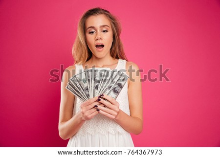 Portrait of a satisfied pretty girl counting money banknotes isolated over pink background