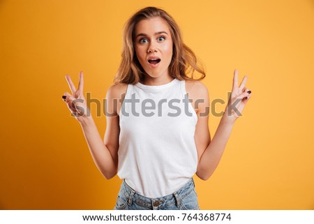 Portrait of a cheerful young girl showing peace gesture and looking at camera isolated over yellow background Royalty-Free Stock Photo #764368774