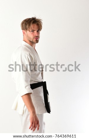 Guy poses in white kimono with black belt. Healthy lifestyle and jujitsu concept. Man with serious face and bristle isolated on white background, copy space. Karate fighter with fit strong body