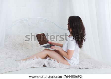 A girl sits on a bed with a laptop on her lap on a white background