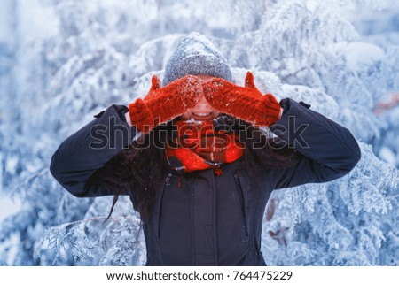 Winter girl in red gloves and scarf blowing snow. Beauty Joyful Teenage Model Girl having fun in winter park. Beautiful girl laughing outdoors. Enjoying nature.
