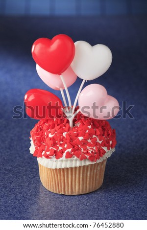 Colorful birthday cupcake with small toy-balloons on blue background (studio shot)