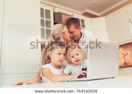 Young happy family using laptop while sitting at kitchen at home. Little children girl watching cartoons with parents