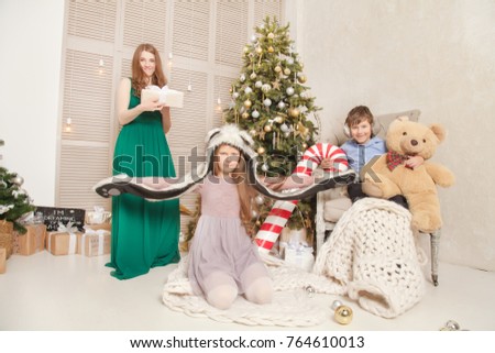 A real family, mother, daughter and son, are happy and have a nice time near the Christmas tree and gifts at home in the room