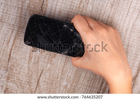 A smartphone with a broken screen in the girl's hand on a wooden table. Close-up. Studio lighting.