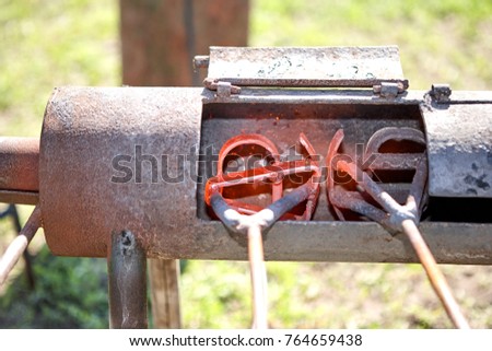 Two branding irons heating in a burner in a field glowing red hot ready to be applied to livestock Royalty-Free Stock Photo #764659438