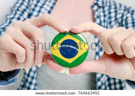 Flag of Brazil printed on button badge, holding by woman in her beautiful hands. Royalty-Free Stock Photo #764663902