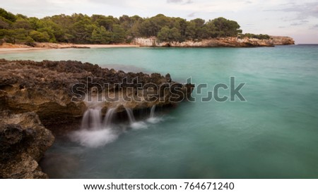 Water flows from a rock pool at Cala Turqueta, Menorca Royalty-Free Stock Photo #764671240