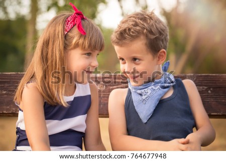 First love. Little sweet boy and a girl sitting on a  bench in the park and having fun. Happy young couple in love outdoor