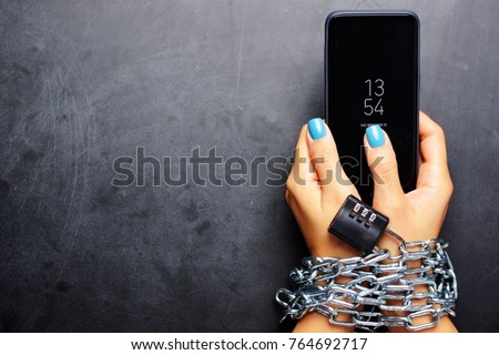 Woman hands tied with metallic chain with padlock on dark background suggesting internet or social media addiction Royalty-Free Stock Photo #764692717
