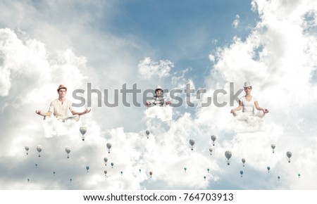 Young family keeping eyes closed and looking concentrated while meditating among flying aerostats in the air with cloudy skyscape on background.
