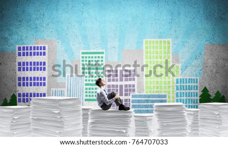 Thoughtful businessman looking away while sitting on pile of documents with drawn cityscape on background. Mixed media.