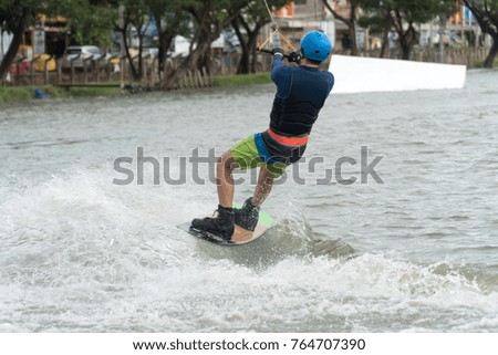 The back of the young man wake boarding on a lake with cable in Bangkok Thailand. Concept sport and leisure activities.