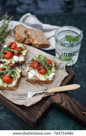 Set bruschette with grilled cherry tomatoes avocado,mozzarella and glass of water on a dark green background
