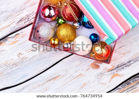 Different shiny Christmas balls in gift box. Christmas decoration toys in open striped gift box on vintage wooden background, top view.
