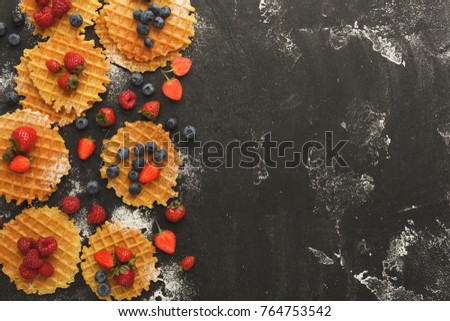 Belgium waffles with berries on black background sprinkled with flour. Border of checkered cookies top view with copy space. Cooking sweet food and tasty breakfast concept