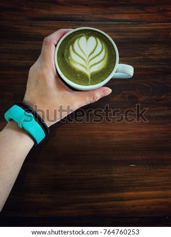 Green tea latte art cup in hand on the wooden table background. Hand holding green tea latte cup, love green tea