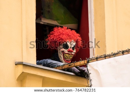Mean, Scary Clown Mask Showing Sharp Teeth and Red Hair in Window of Building
