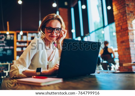 Portrait of successful businesswoman using laptop for distance job sitting in cafe with wifi, attractive female freelancer enjoying  free working schedule looking at camera uploading software