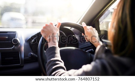 Female hands on the steering wheel of a car while driving. sunset the background, the windshield and road Royalty-Free Stock Photo #764807152