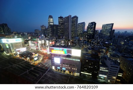 Night skyline of modern high-rise skyscrapers with railroad tracks stretching by crowded buildings and city lights & billboard signs glistening under sunset sky in Shinjuku District, Tokyo, Japan