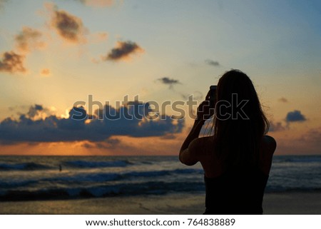 silhouette of young attractive female making photo of sunset by smartphone