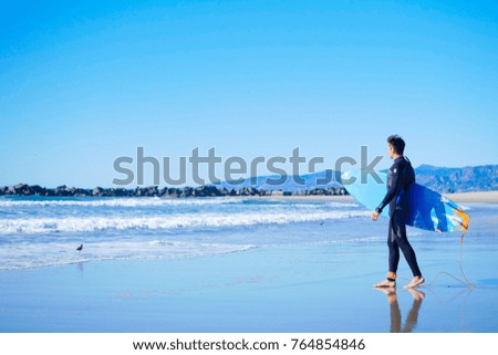 Male american surfer wearing full black wetsuit going to surf in Pacific ocean Royalty-Free Stock Photo #764854846