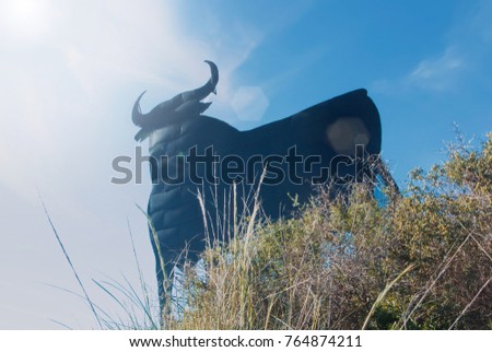 Toro Osborne, iconic symbol of Spain, silhouette of black bull on the hill with green bush at the foreground.