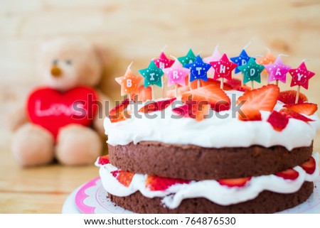 Homemade chocolate whipping cream with strawberry fruit cake decorate colorful candle with cute teddy bear and red love heart on wooden table background ,Happy Birthday party romantic creative design.