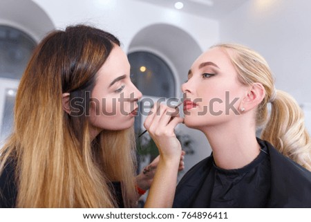 backstage photo as visagiste applying lipstick with brush for young woman in beauty studio