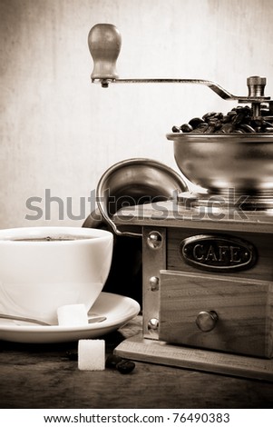 cup full of coffee, beans, pot and grinder on wooden background
