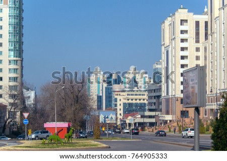 View of Almaty streets. Residential & business district, green installation of deers, cars, modern buildings & some smog above the city. Selective focus