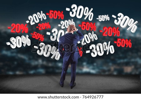 View of a Businessman in front of a wall with sales promotion 20% 30% and 50% flying on an interface - Shopping concept