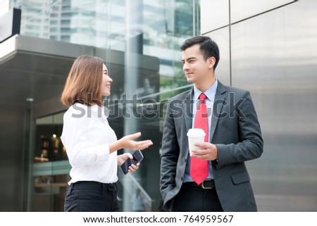Handsome Colombian Businessman and Asian businesswoman standing and having small talk outside office building in the morning before work