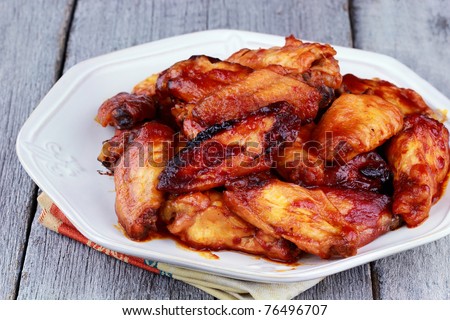 Plate of delicious barbecue chicken wings with shallow depth of field on a rustic background.