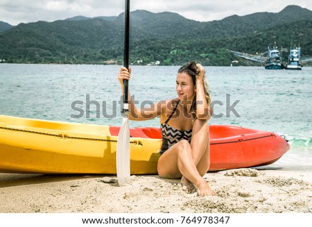 a girl in a swimsuit is sitting on the beach with a canoe