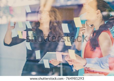 business, startup, planning, management and people concept - happy creative team writing on stickers at office glass board Royalty-Free Stock Photo #764981293