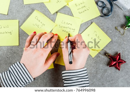 Girl writing new years resolutions, hands in picture. Grey stone table with colorful sticky notes with popular new year resolutions and pen, copy space