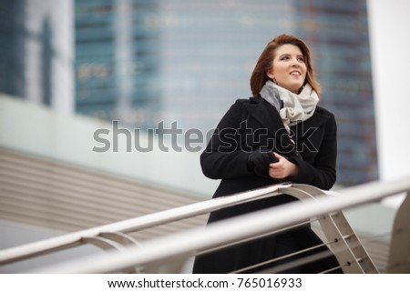 Photo of smiling woman in black coat and scarf on blurred background