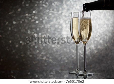 Picture of bottle with flowing champagne in wine glasses on gray background