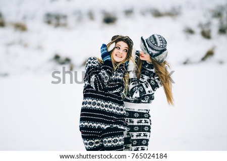 Couple of young women. Girl wears warm hat girl closes friend's ears with her hands in mittens in cold winter